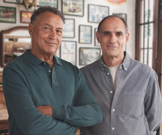 Two older men standing side by side both looking at the camera